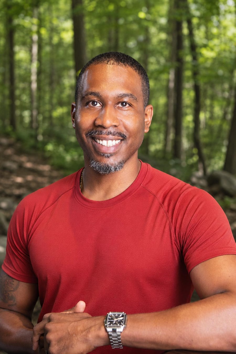 James, founder of Ascend Bro Hikes™, smiling in a red trail shirt in a green hardwood forest
