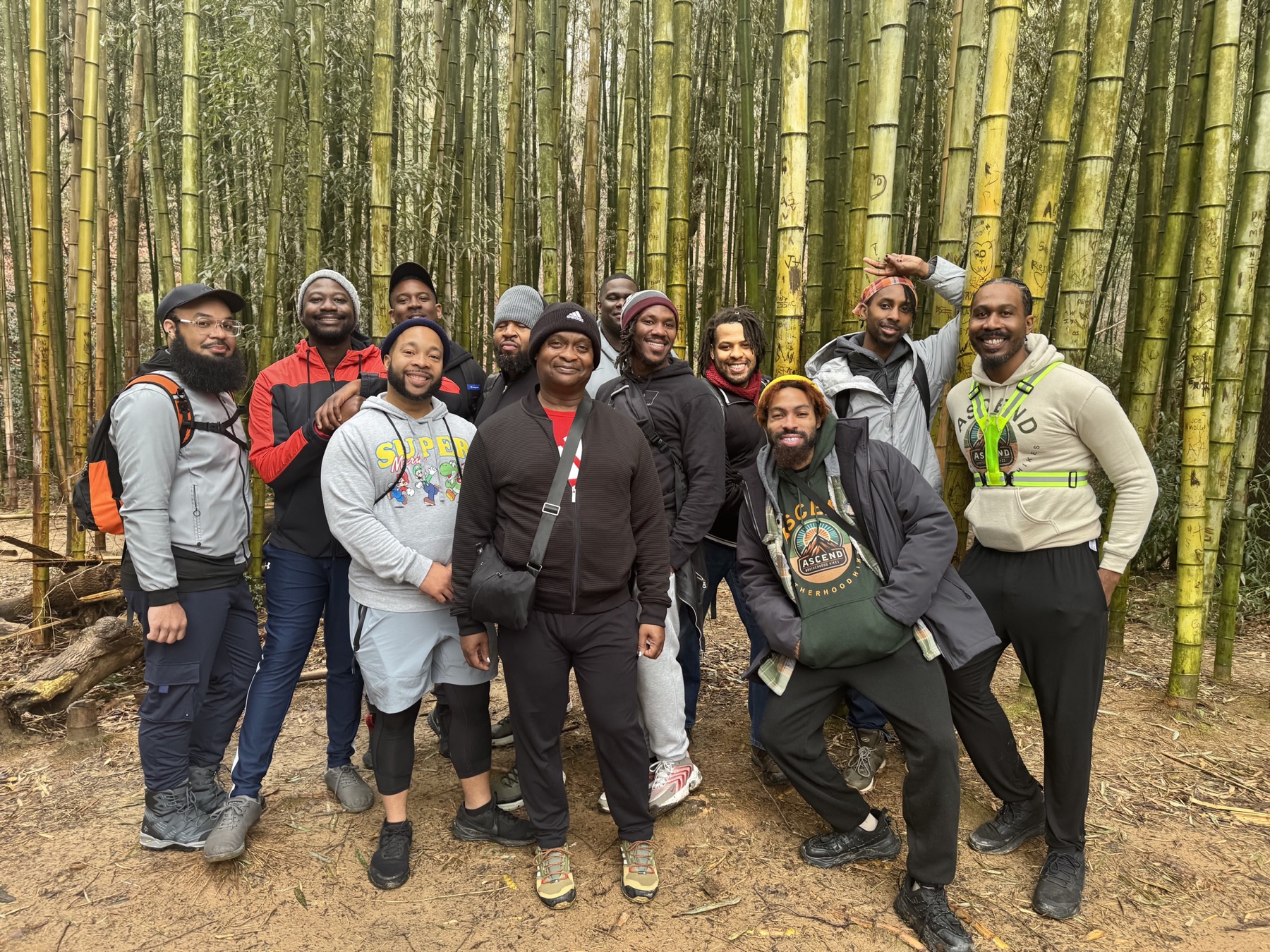 Black men in hiking layers pose together in front of a tall bamboo grove.