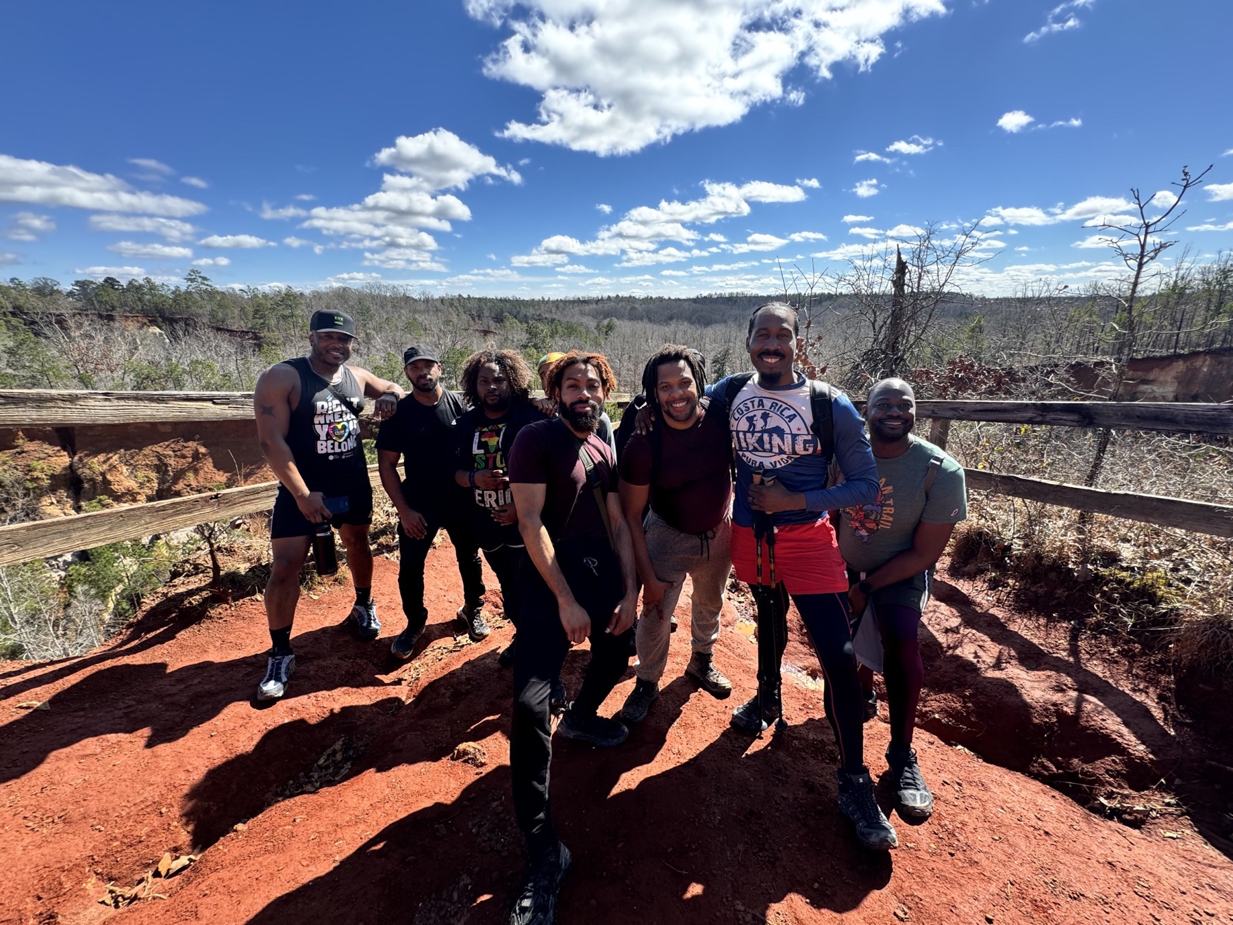 Black men stand shoulder to shoulder on a sunny red-clay overlook.