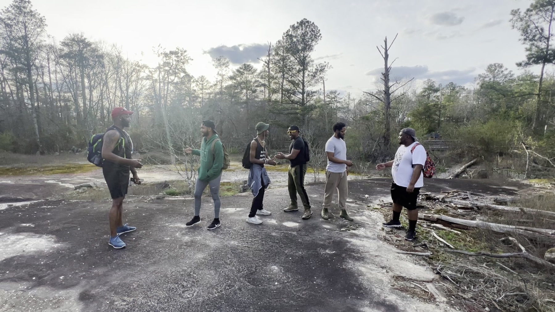 Black men stand in a loose circle on a wide granite outcrop lit by low afternoon sun.