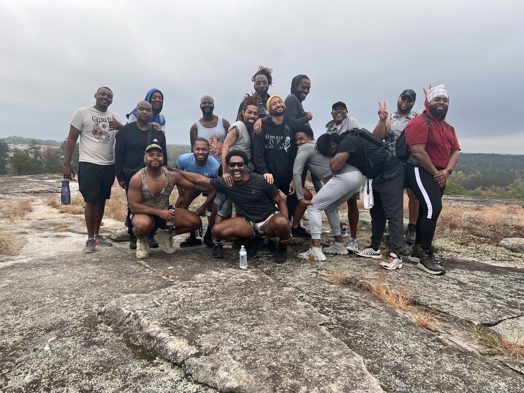 A large group of Black men pose together on a misty granite summit.