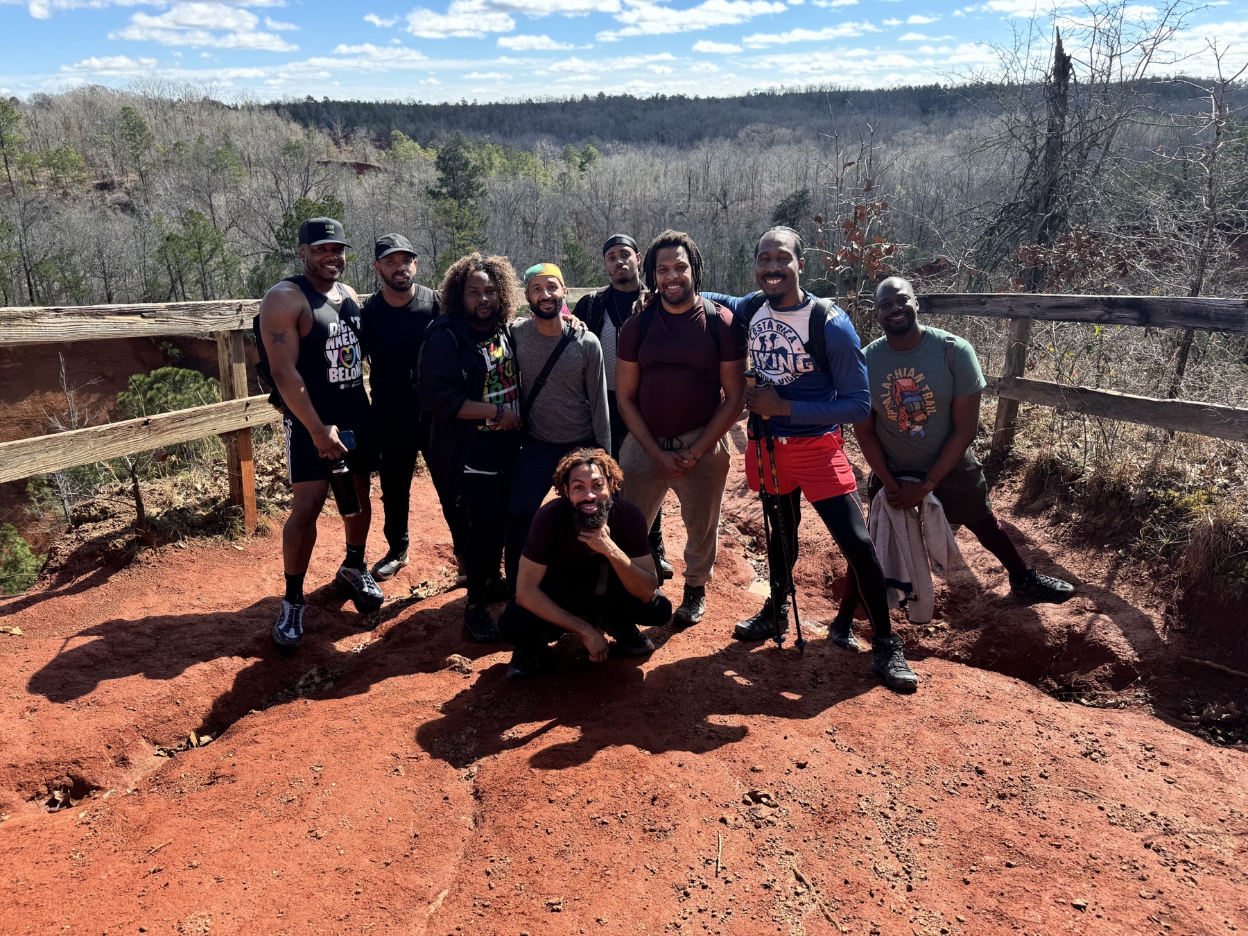 Black men pose on red clay above a wooded canyon on a clear winter day.