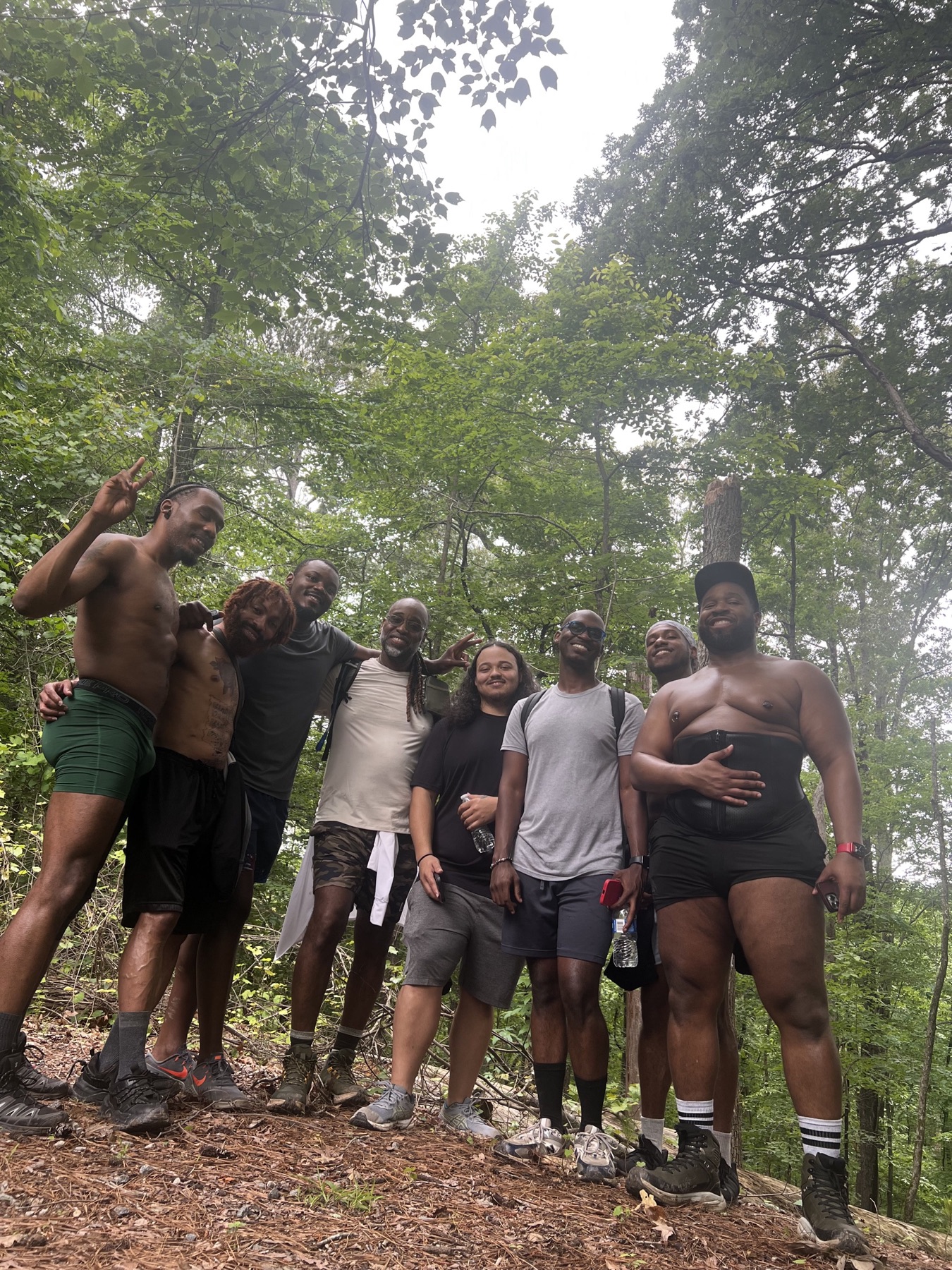 Black men smile and pose on a wooded ridge after a steep hike.
