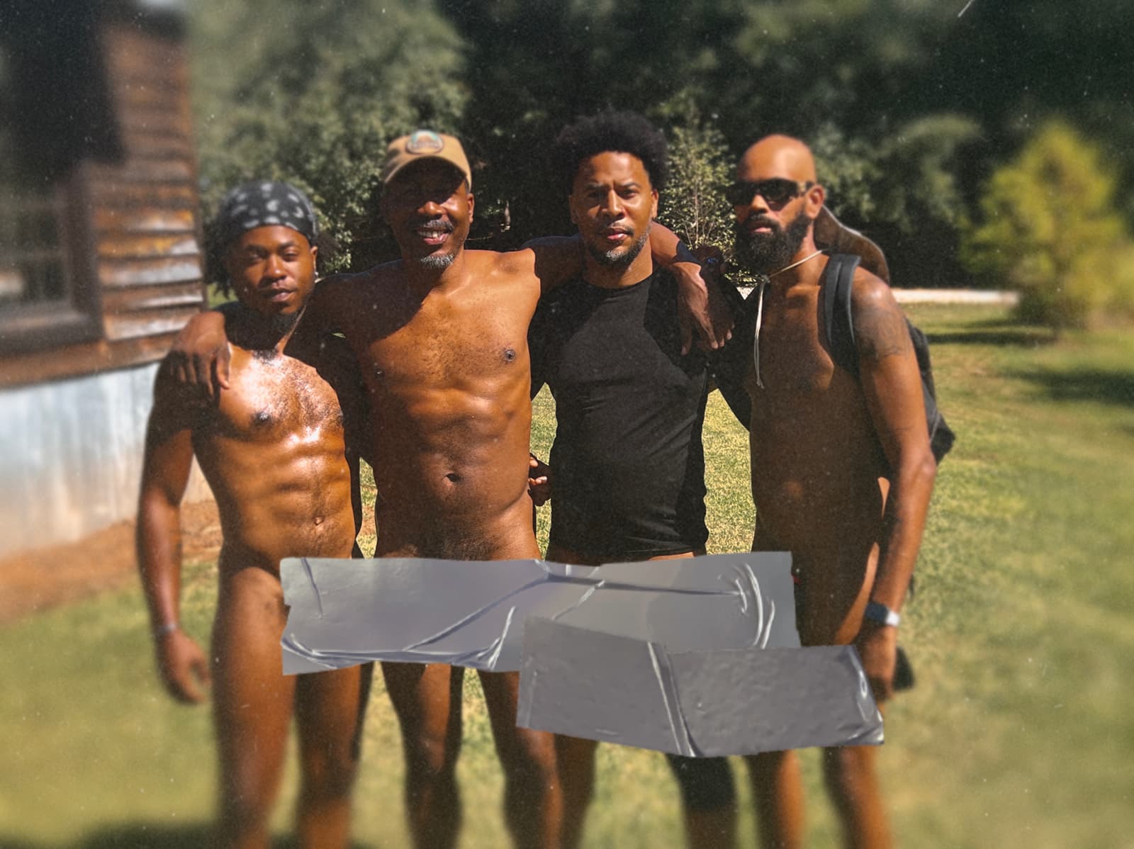 Four adult Black men in clothing-optional attire stand close together beside a cabin and trees.