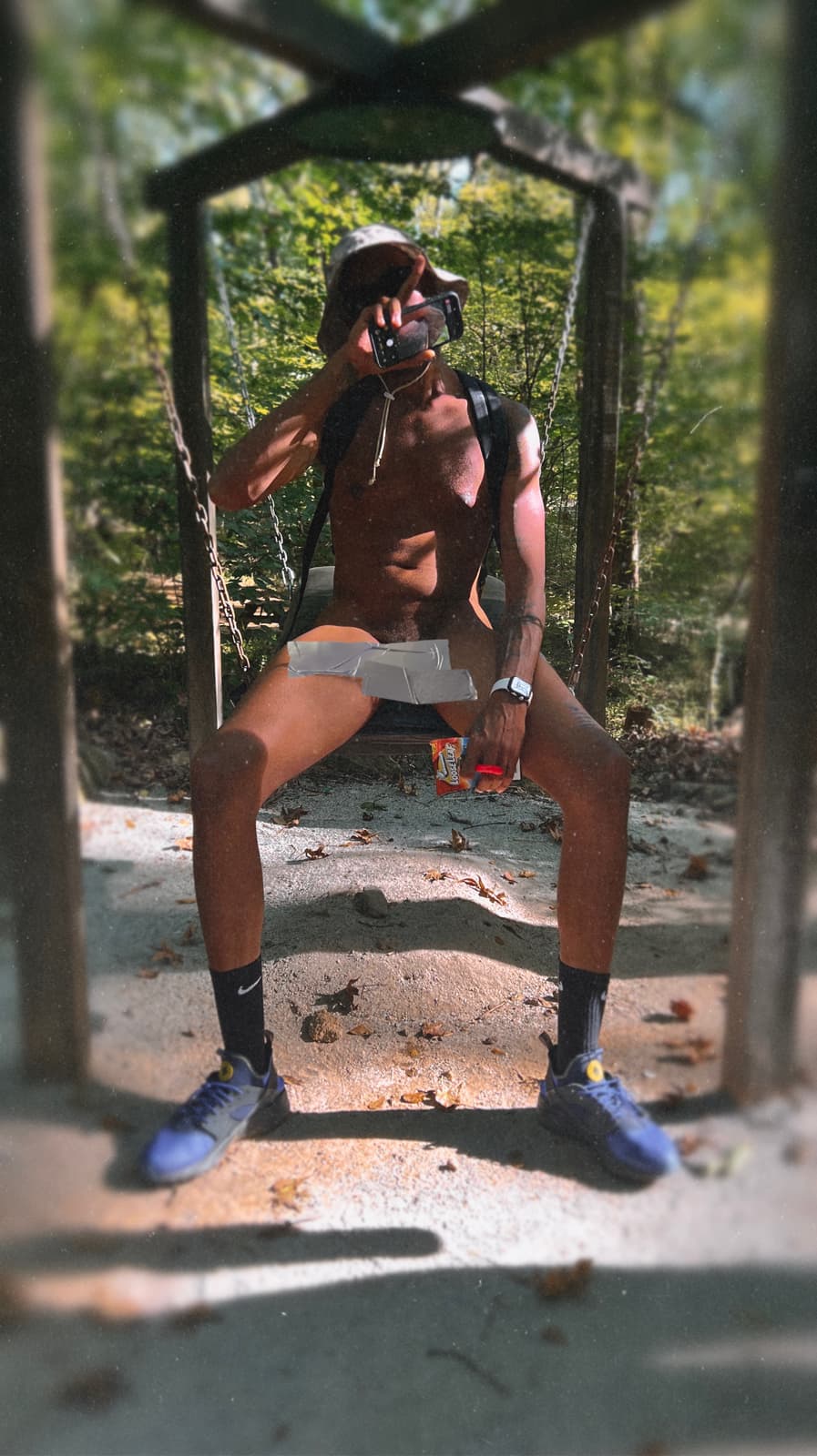 An adult Black man in clothing-optional attire sits beneath a small wooden trail shelter in the forest.