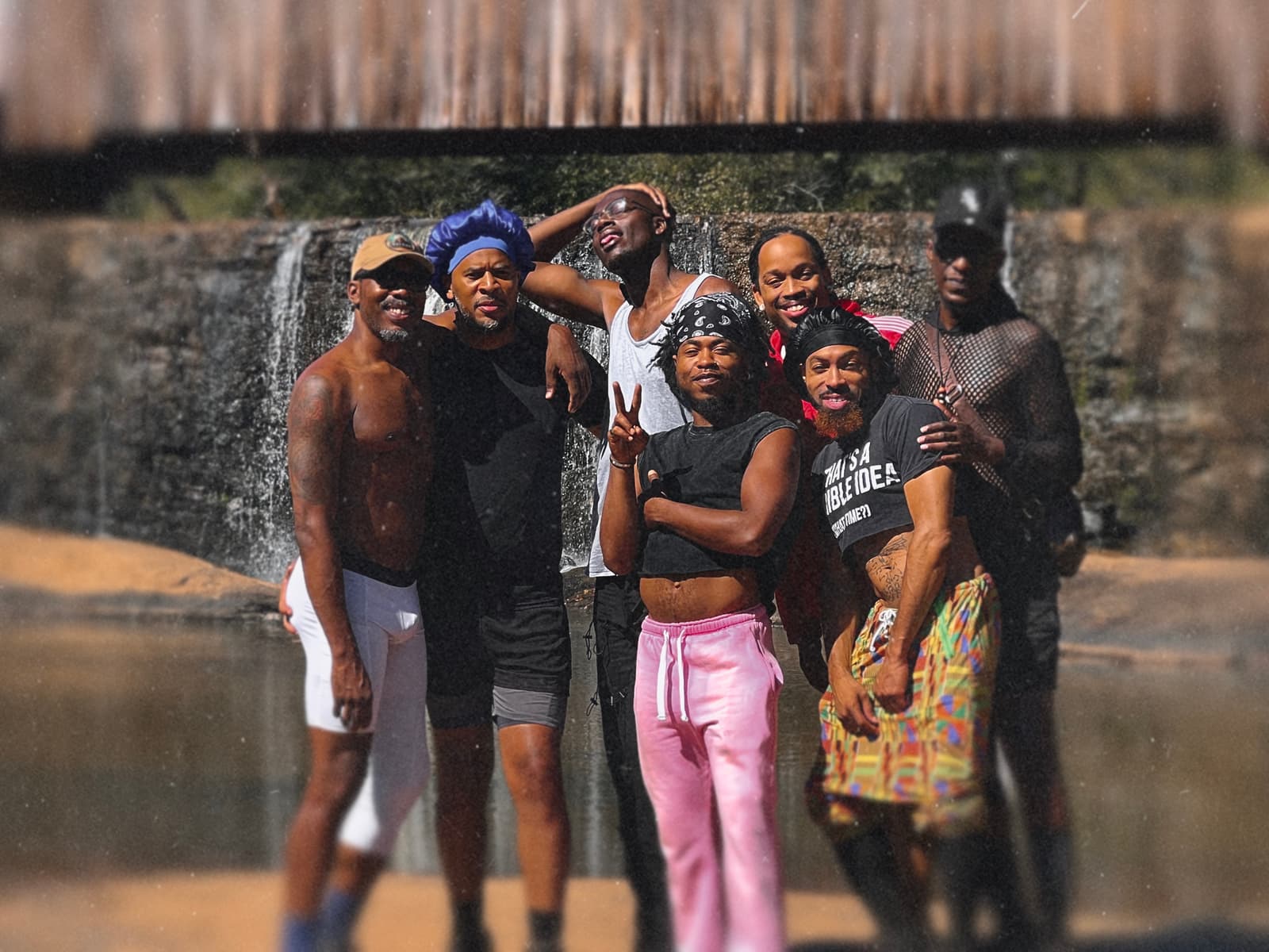 Seven Black hikers smile together in front of the low waterfall at Watson Mill Bridge State Park.