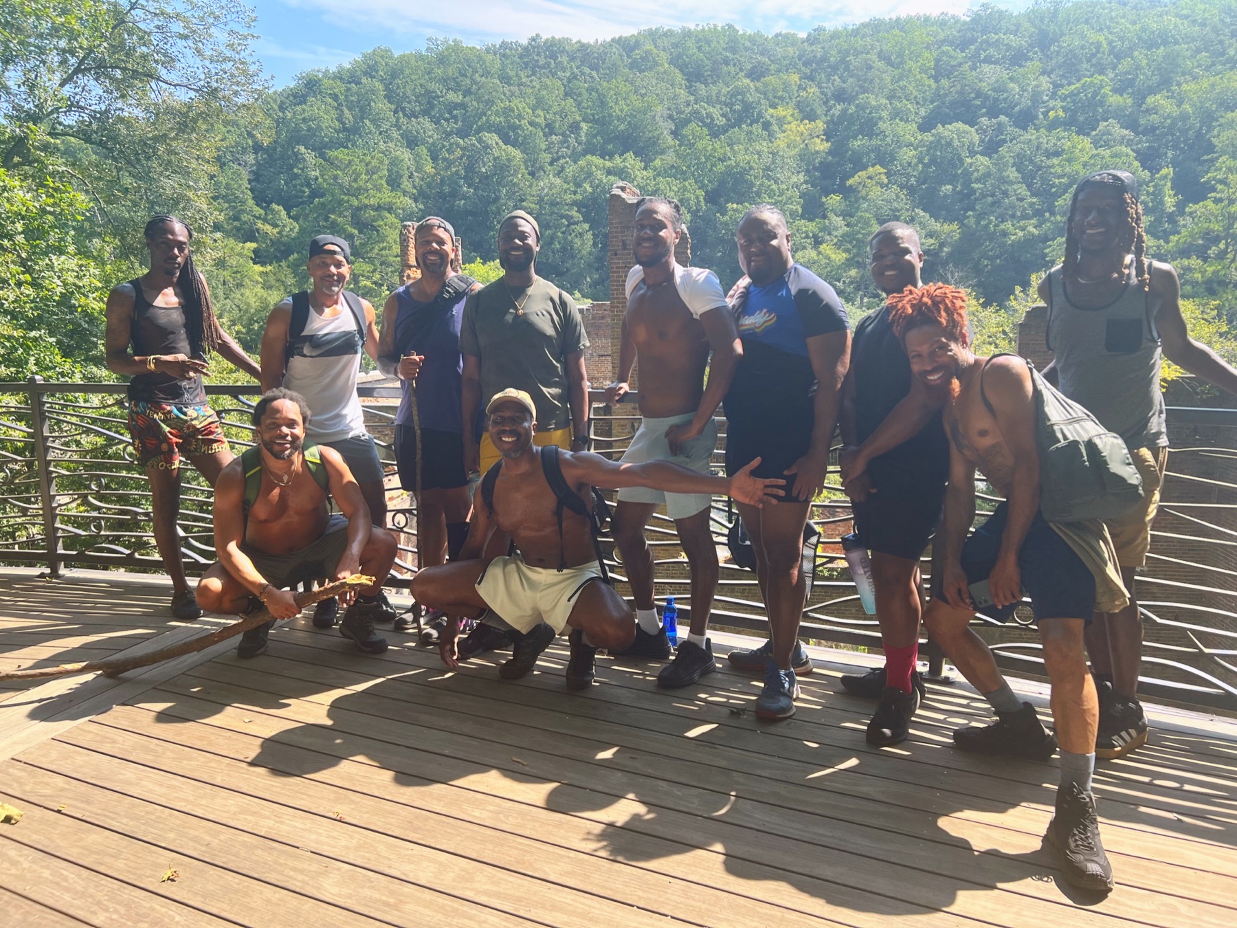 Black men stand and kneel together on an overlook above historic brick ruins and green hills.