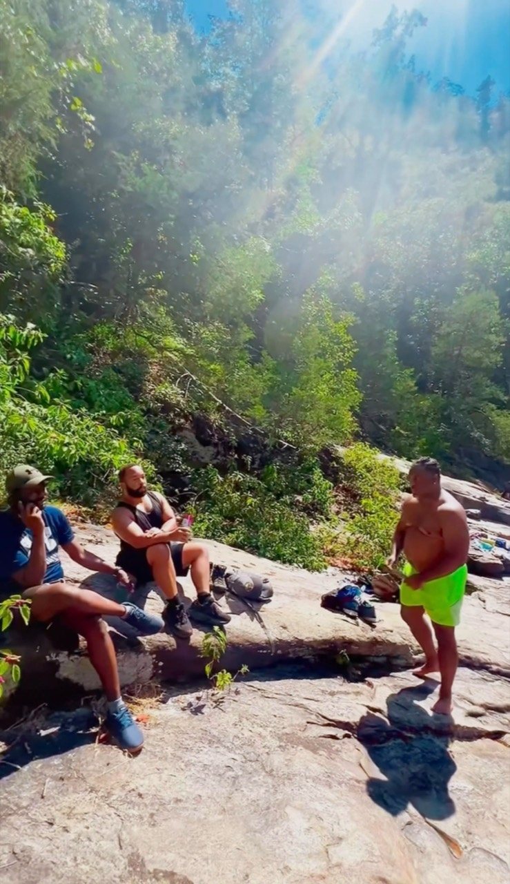 Three hikers pause with their packs on broad sunlit rock surrounded by dense forest at Tallulah Gorge.