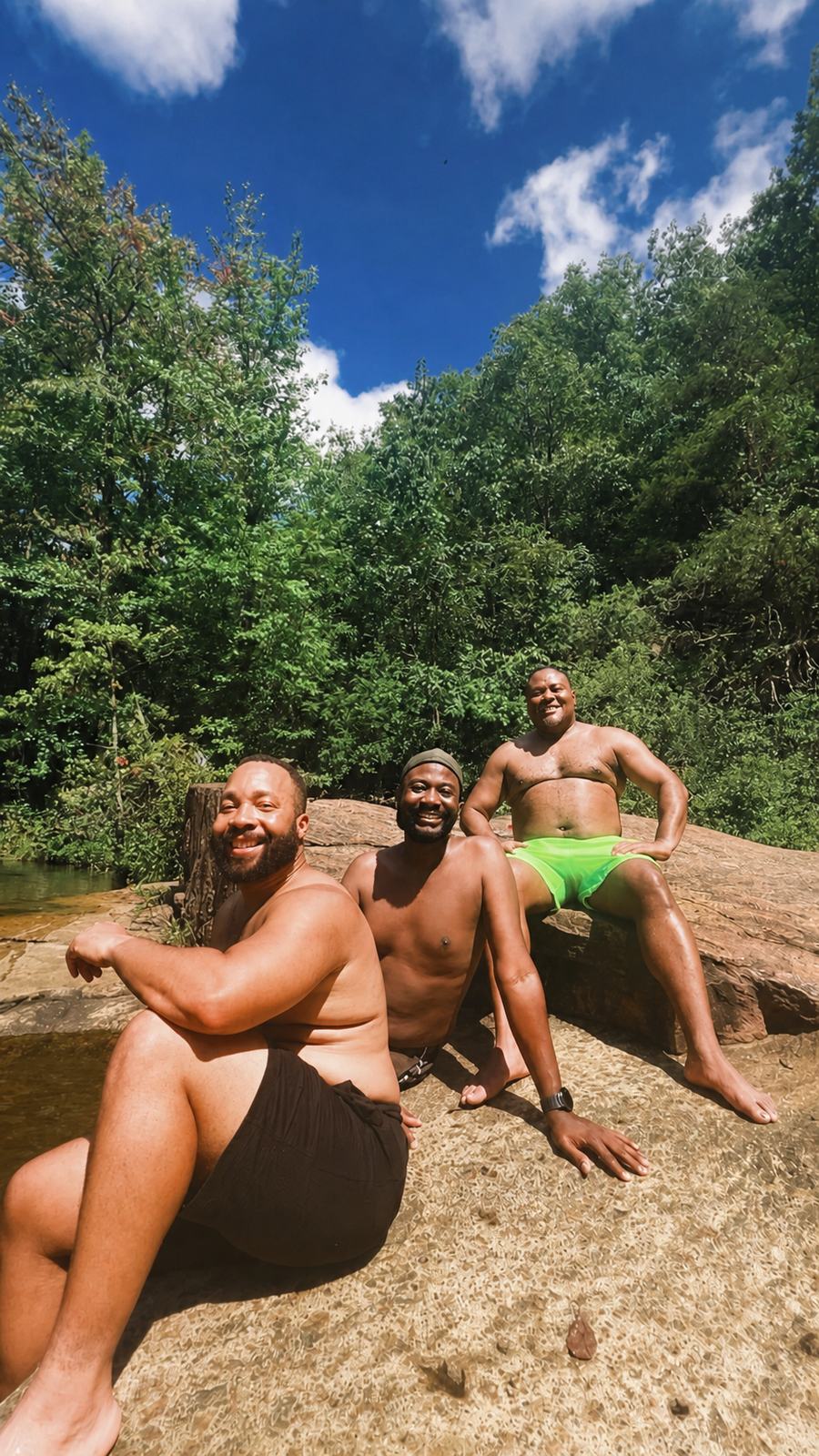 Three Black hikers sit together on sun-warmed rock beside a forest swimming hole at Tallulah Gorge.