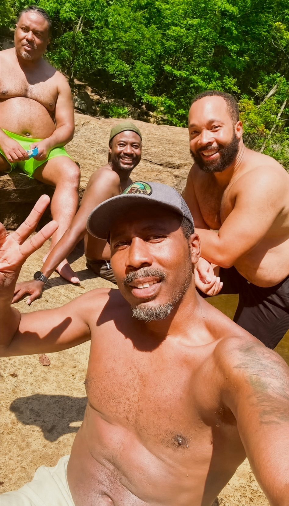 Four Black hikers crowd into a sunny selfie on the rocks beside a forest swimming hole at Tallulah Gorge.