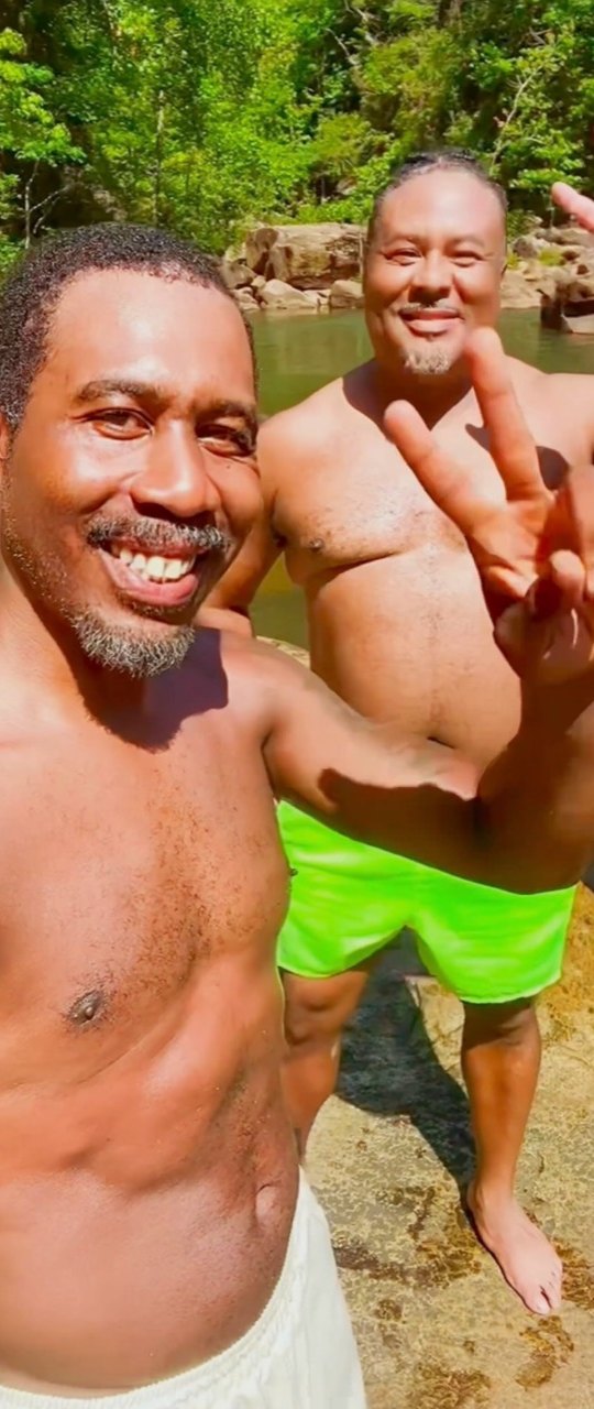 Two Black hikers smile and flash peace signs beside a forest swimming hole at Tallulah Gorge.