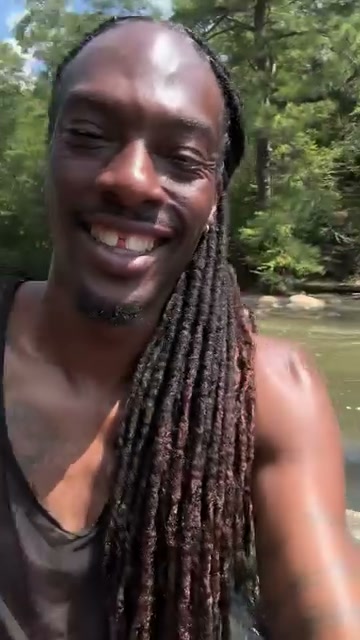Ali smiling beside Sweetwater Creek, with green trees along the water